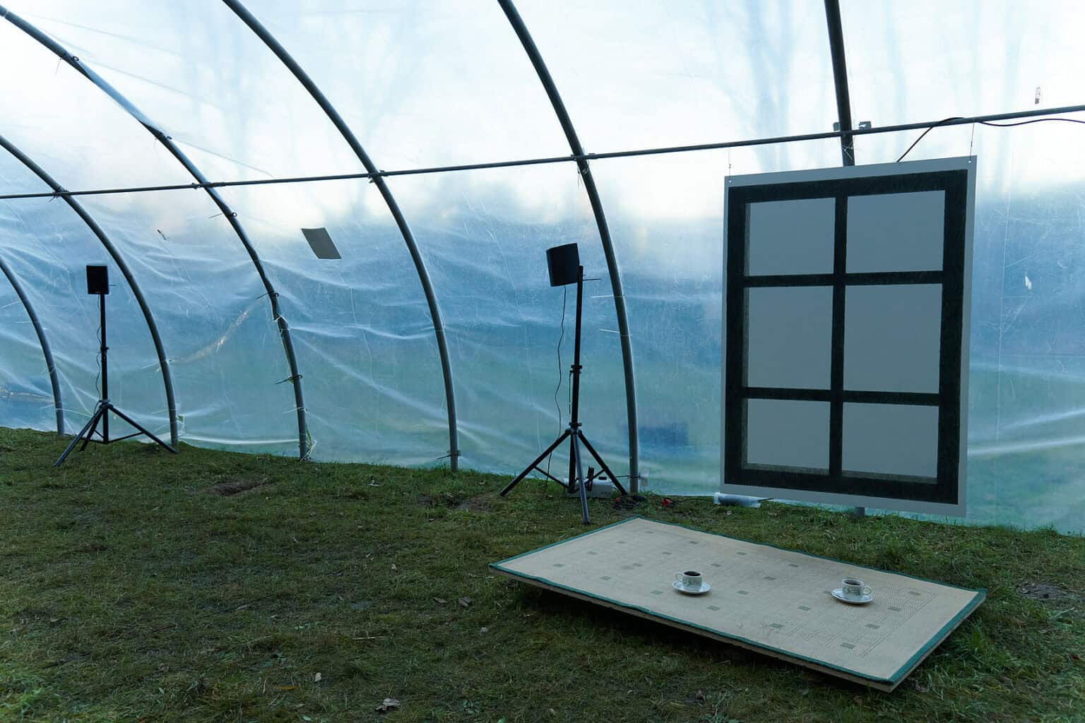 Foto: Ansicht eines mit transparenter Folie abgehangenen Metallkonstruktion, im Außenbereich, auf Rasen. Innerhalb der Konstruktion stehen und hängen Objekte.