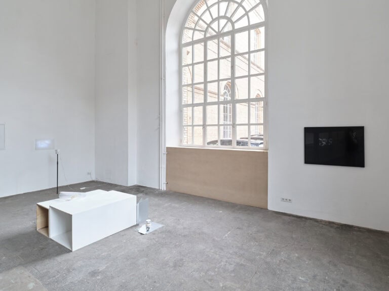 Foto: Heller Ausstellungsraum mit großem Rundbogenfenster. Im Raum stehen bzw. hängen mehrere Kunstwerke auf dem Boden und an den Wänden