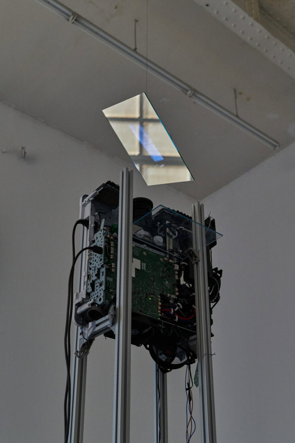 Foto: Detailaufnahme eines an einem Gerüst befestigten Beamers, der auf einen oberhalb des BEamers befestigten, von der Decke hängenden Spiegel projiziert.