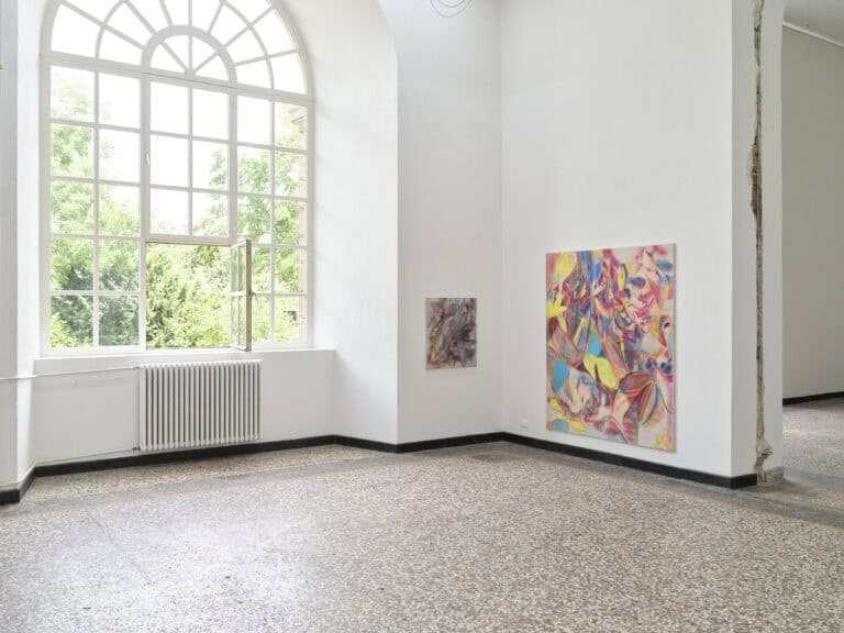 Foto: Heller Ausstellungsraum mit großem Rundbogenfenster. An den Wänden hängen zwei bunte abstrakte Gemälde.