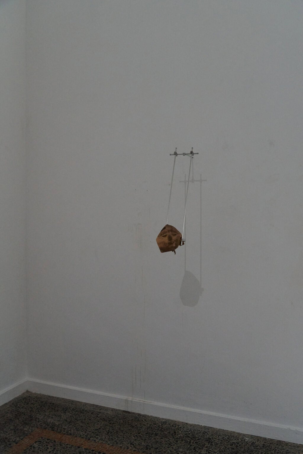 Foto: Ein Raum mit weißen Wänden. An der Wand ein Objekt auf unterschiedlichen Materialien. unterhalb des Objektes bleiche Tropfspuren an der Wand.