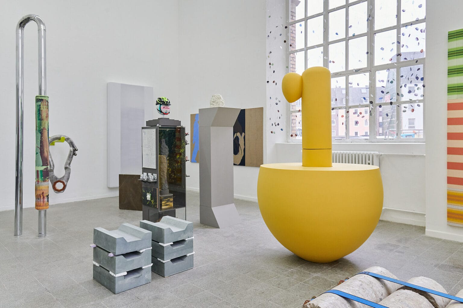 Foto: Ansicht eines Raumes mit weißen Wänden, großen Bogenfenster und grauem, gekachelten Boden. Im Raum und an den Wänden befindet sich eine Vielzahl von großen Objekten, die dicht beieinander stehen.