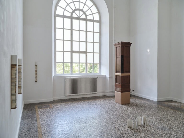 Foto: Heller Ausstellungsraum mit großem Rundbogenfenster. Im Raum stehen bzw. hängen mehrere Kunstwerke auf dem Boden und an den Wänden