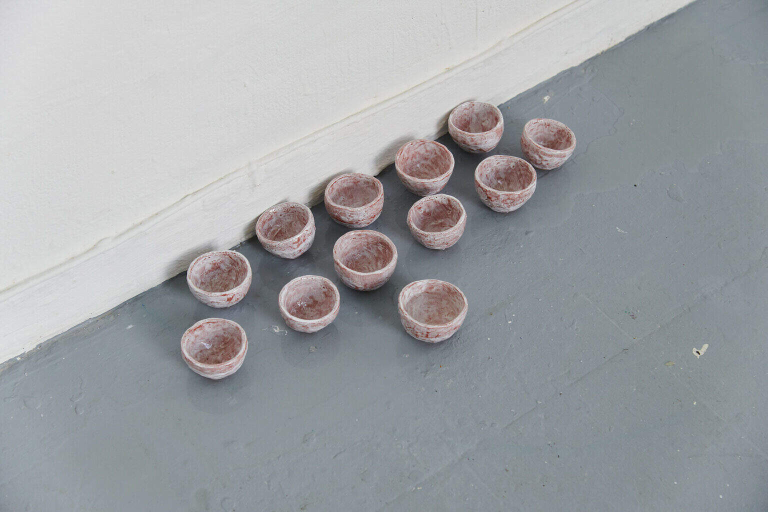 Foto: Detailaufnahme von einer Gruppe kleiner, schalenförmiger Objekte auf grauem Boden.