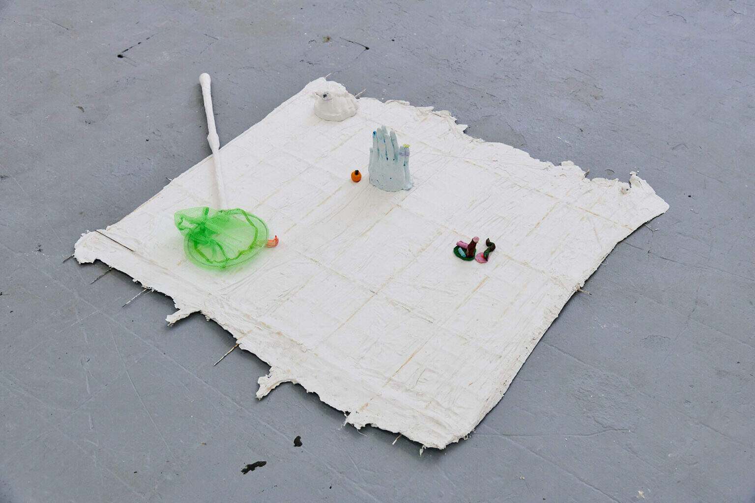 Foto: Detailaufnahme eines Objektes, bestehend aus unterschiedlichen Materialien, auf grauem Boden.