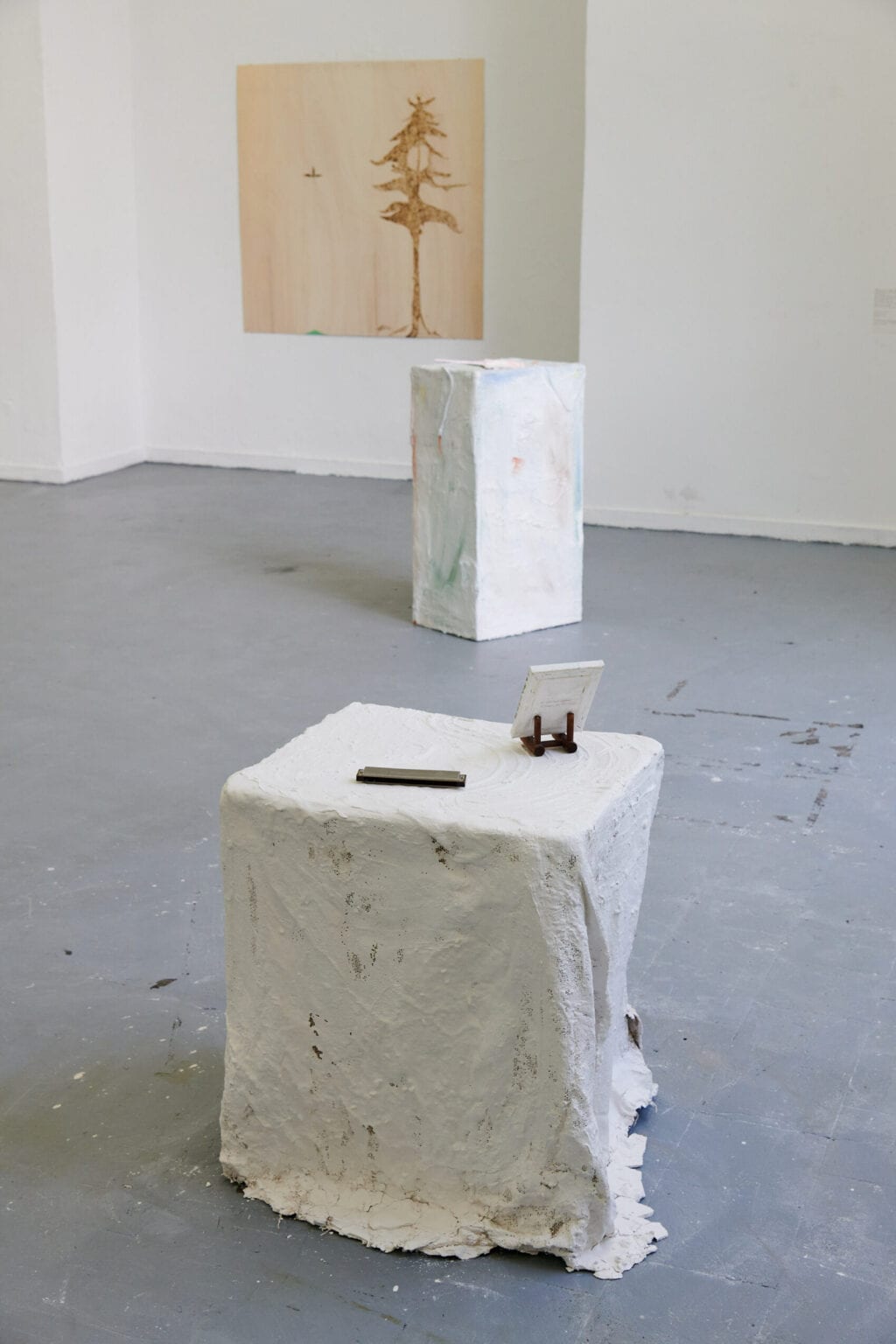 Foto: Ein Raum mit weißen Wände und grauem Boden. Im Raum zwei Objekte. An der Wand ein flaches Objekt.