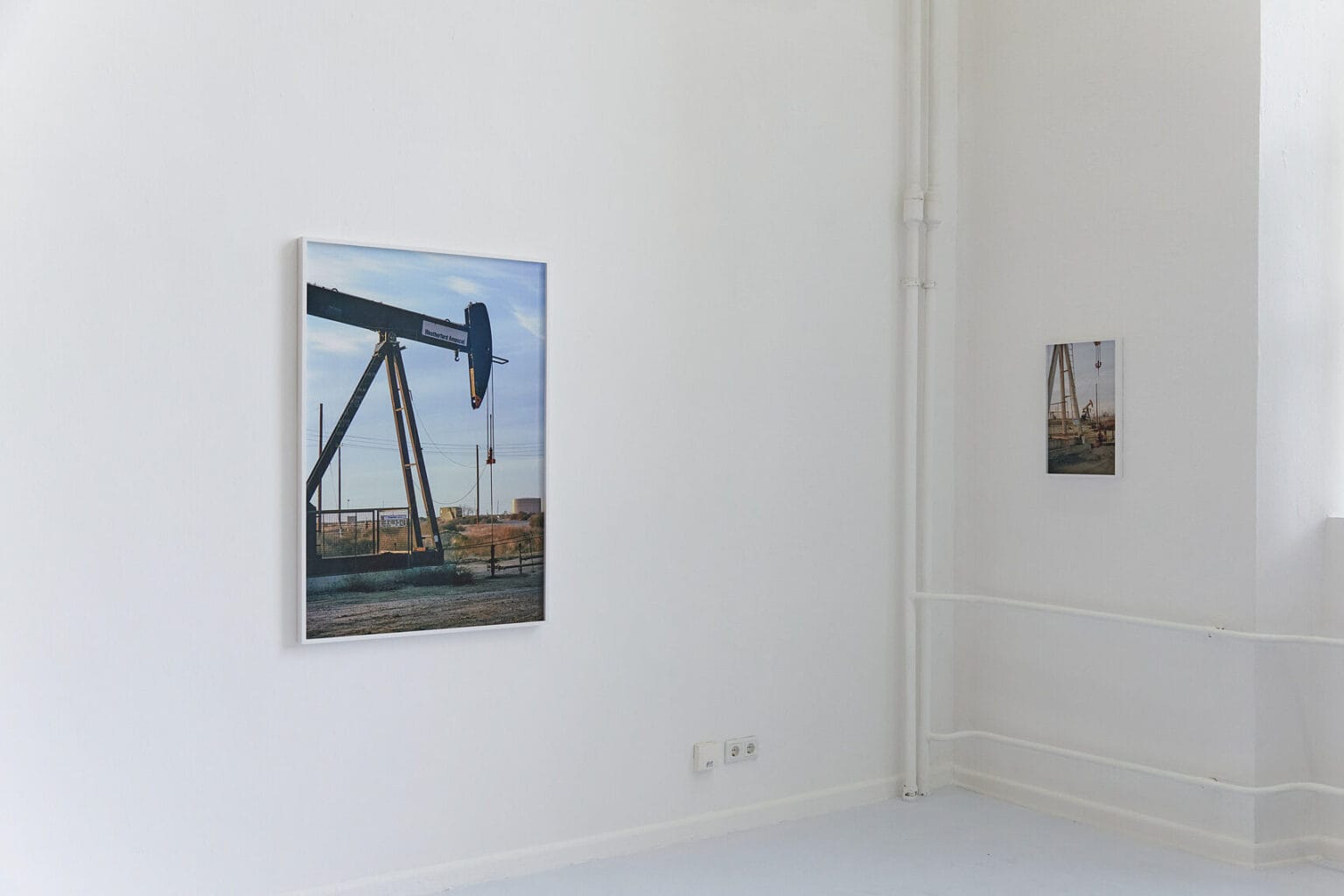 Foto: Eine Raumecke mit weißen Wänden. An der Wand zwei gerahmte Objekte im Klein- und Mittelformat.