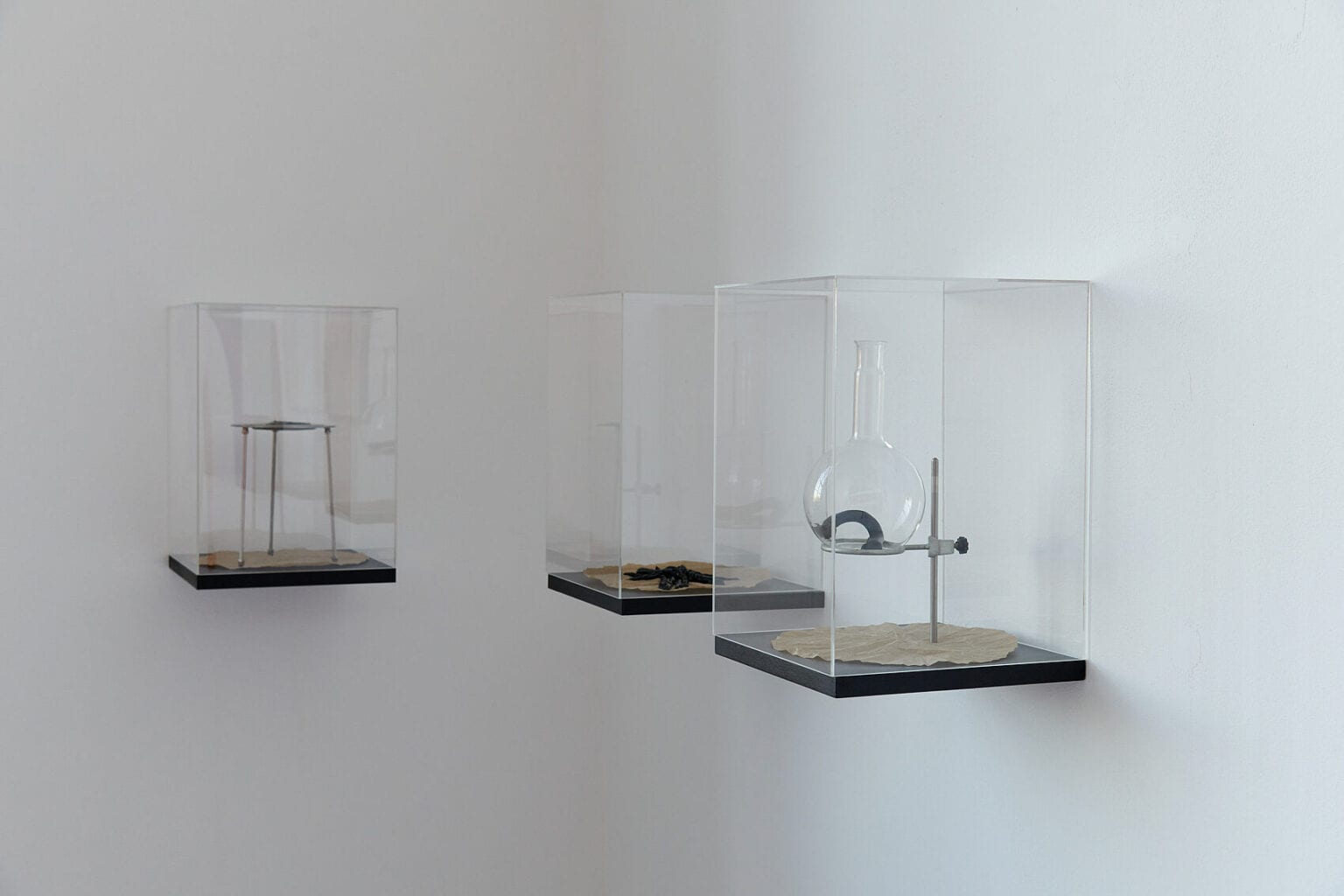 Foto: Nahaufnahme von drei an der Wand montierten Objekten aus unterschiedlichen Materialien in einer Raumecke.