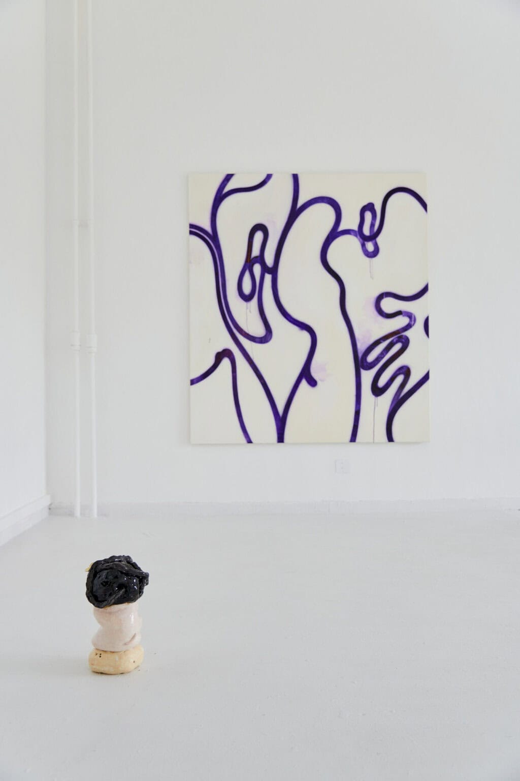 Foto: Die Ecke eines Raumes mit weißen Wänden und weißem Boden. An der Wand eine großformatige Leinwandarbeit. Auf dem Boden steht ein Objekt.