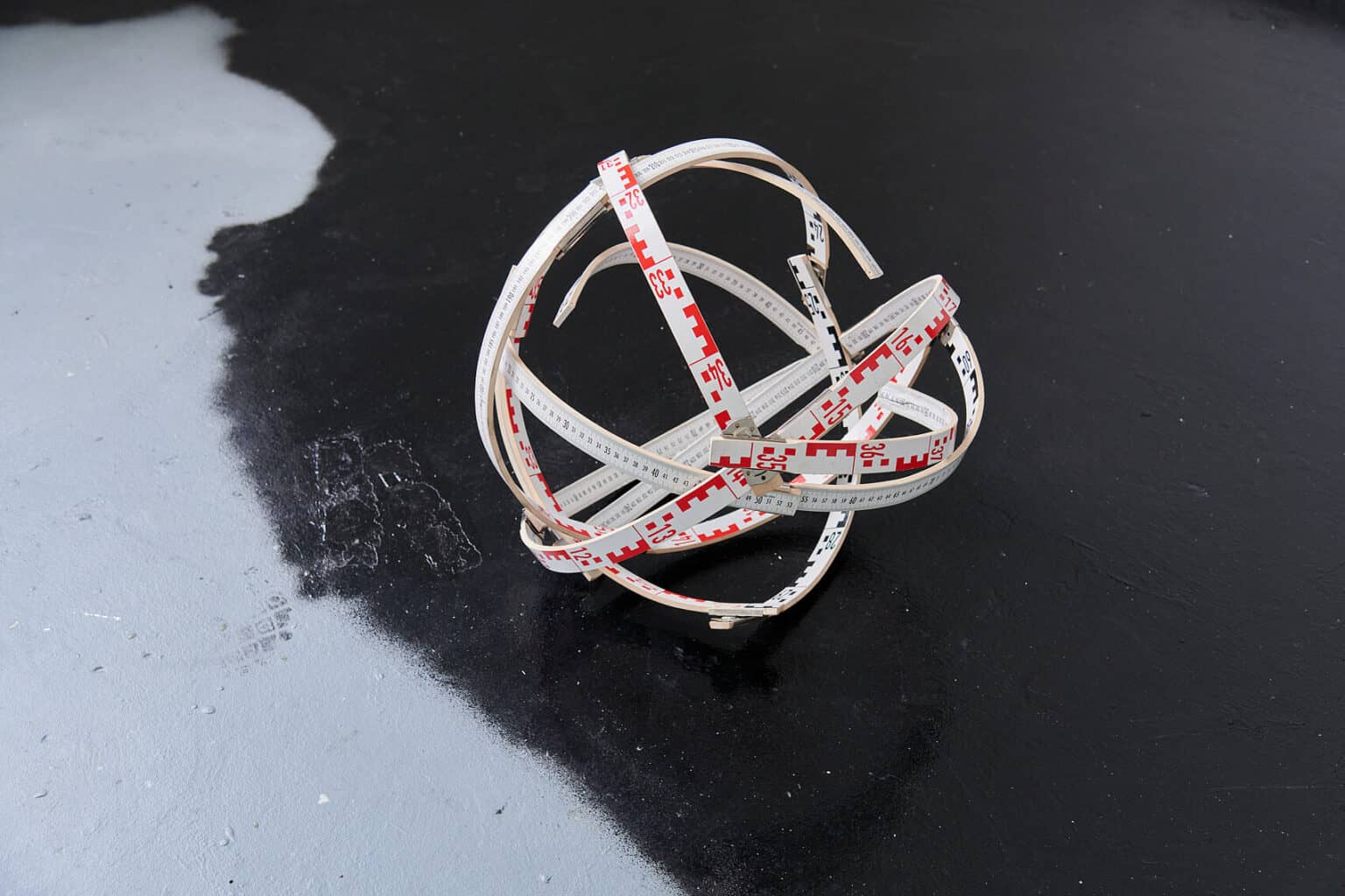 Foto: Eine helle Skulptur auf grau-schwarz gestrichener Oberfläche.