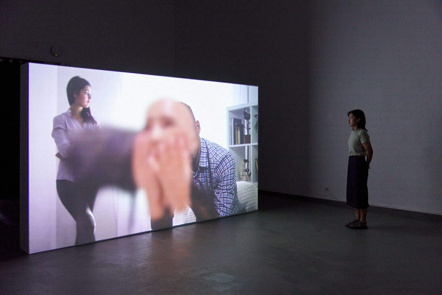 Foto: Ein abgedunkelter Raum. Auf dem Boden steht ein großer, eingeschalteter Bildschirm. Im Raum steht ein Mensch.