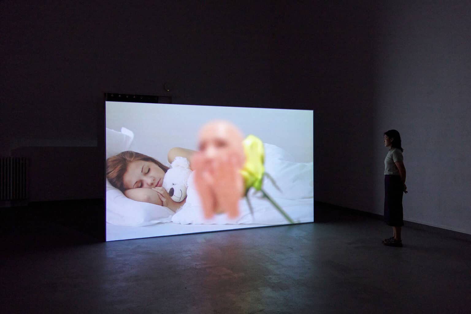 Foto: Ein abgedunkelter Raum. Auf dem Boden steht ein großer, eingeschalteter Bildschirm. Im Raum steht ein Mensch.