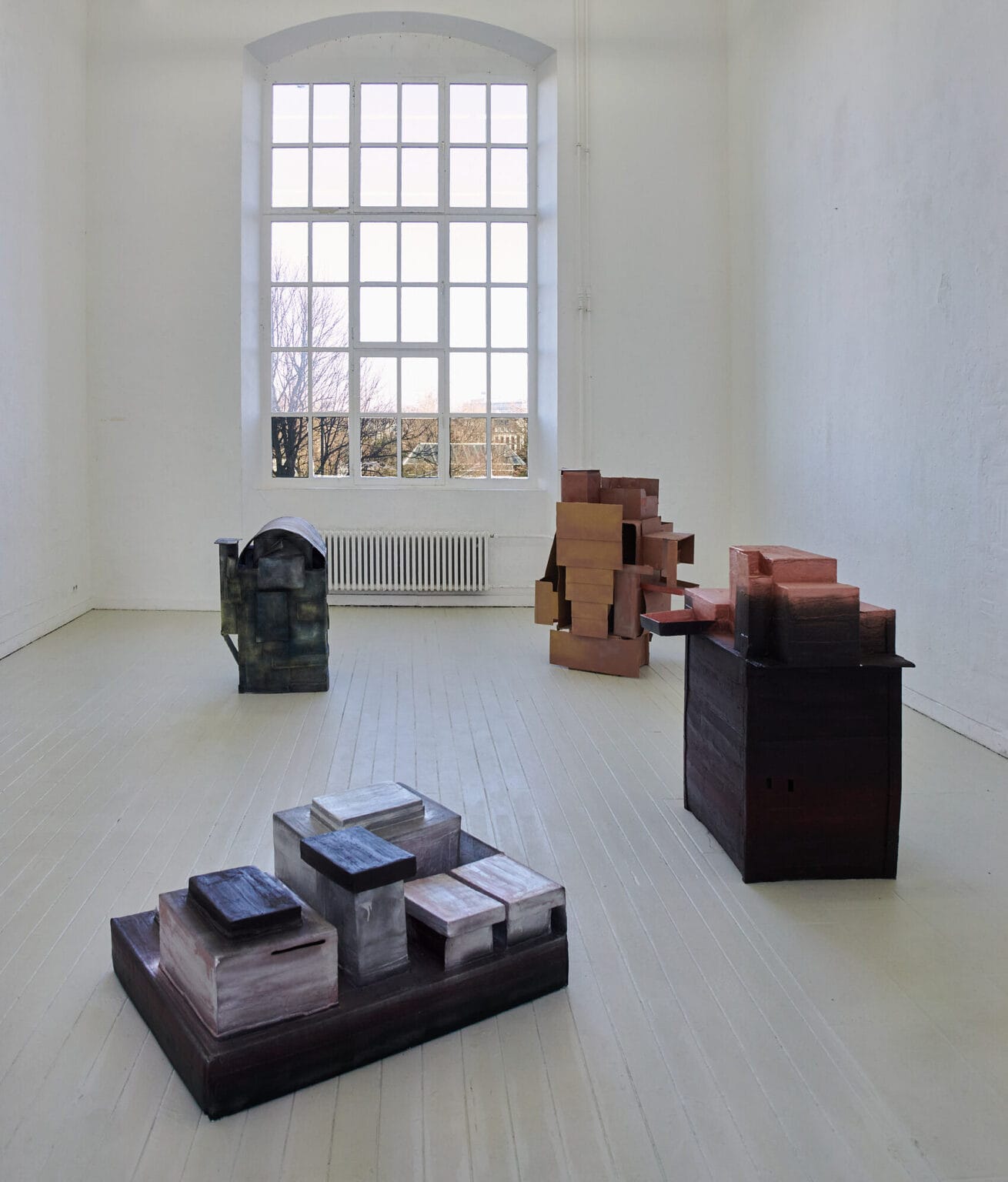 Foto: Ansicht eines Raumes mir weißen Wänden und hellem Dielenboden. Im Raum stehen vier große, verschachtelte, kastenförmige Objekte.