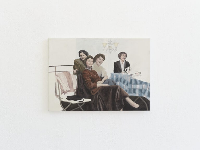 Foto: Detailaufnahme von einem Gemälde an einer weißen Wand. Das Gemälde zeigt vier Frauen, die an einem Tisch sitzen.
