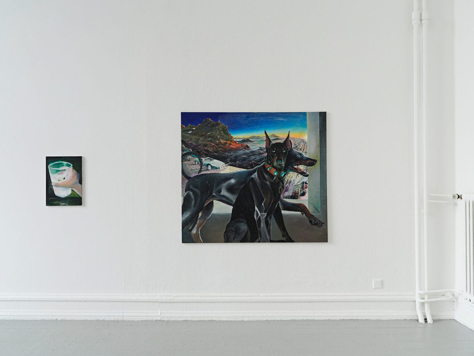 Foto: Ansicht eines Raumes mit weißen Wänden und grauem Boden. An der Wand hängen zwei Leinwandarbeiten im Klein- und Mittelformat.