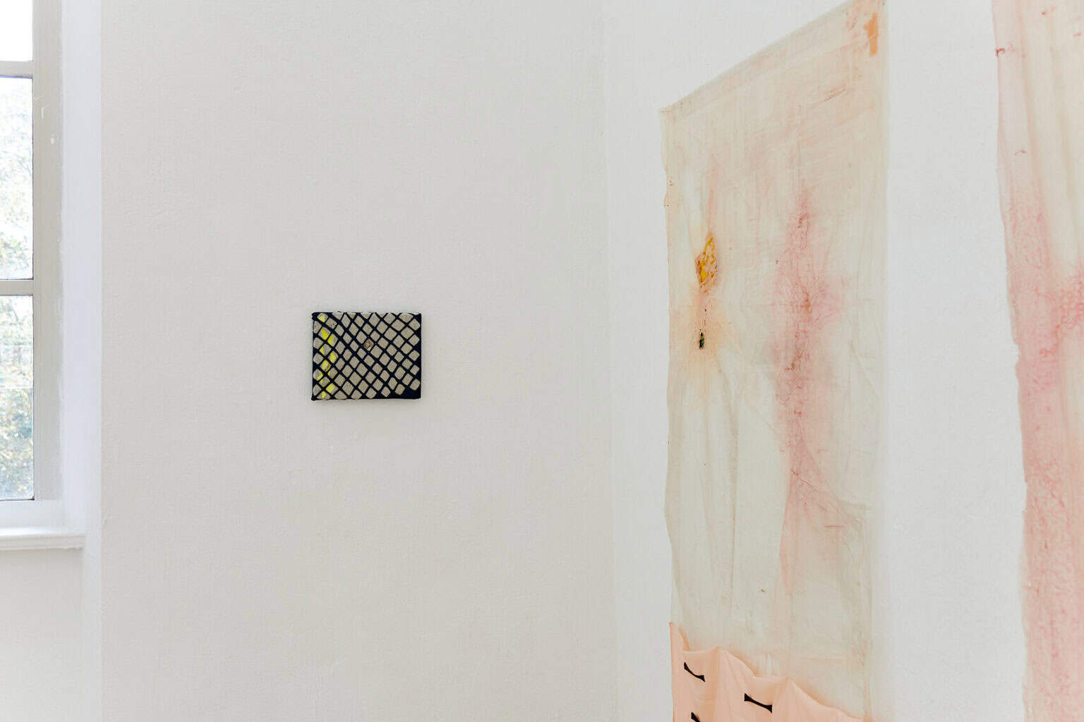 Foto: Eine Raumecke mit weißen Wänden. An der Wand hängen Objekte im Klein- und Großformat.