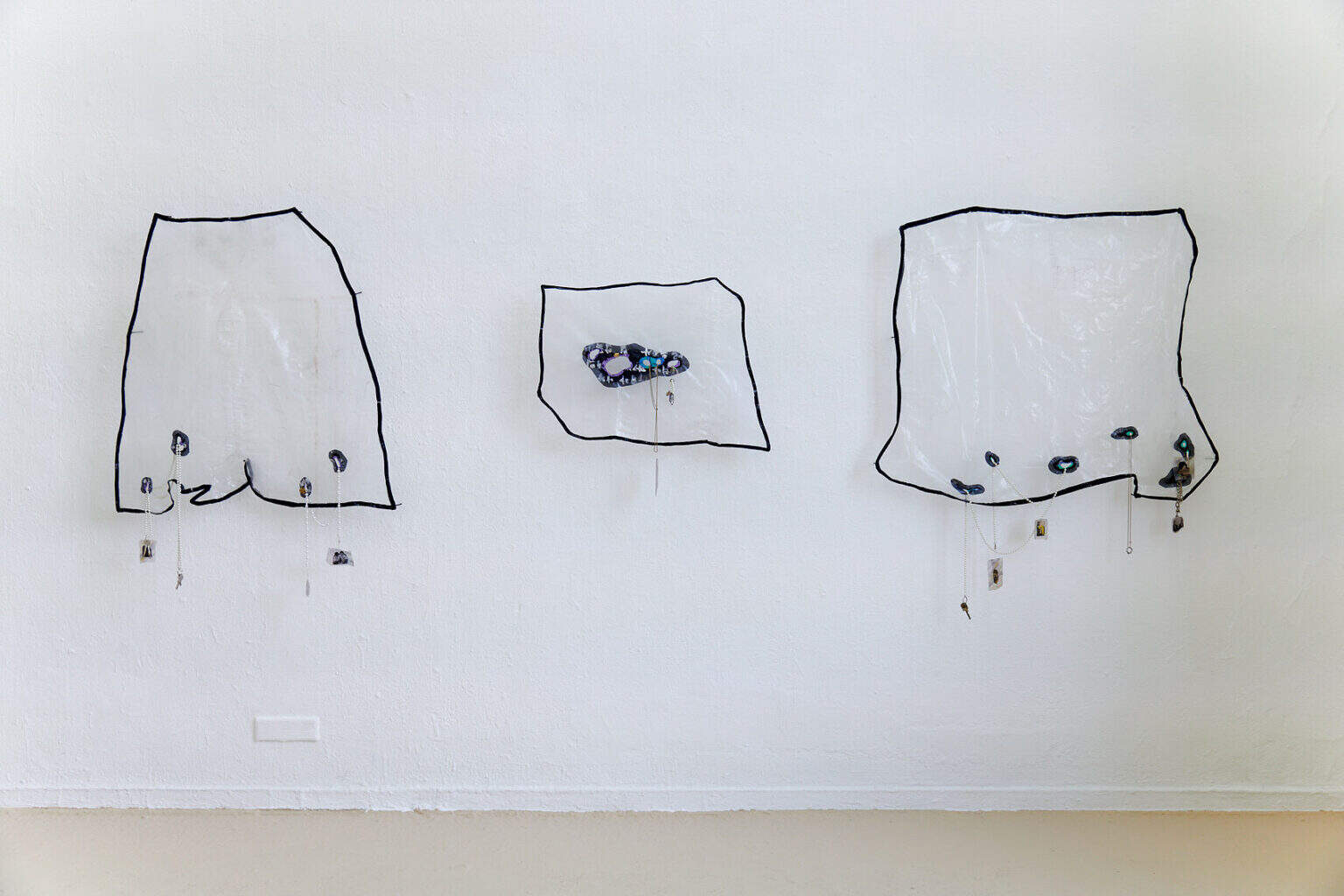 Foto: Ein Raum mit weißen Wänden und beigem Boden. An der Objekt eine Gruppe aus drei Objekten, die auf gleicher Höhe hängen.