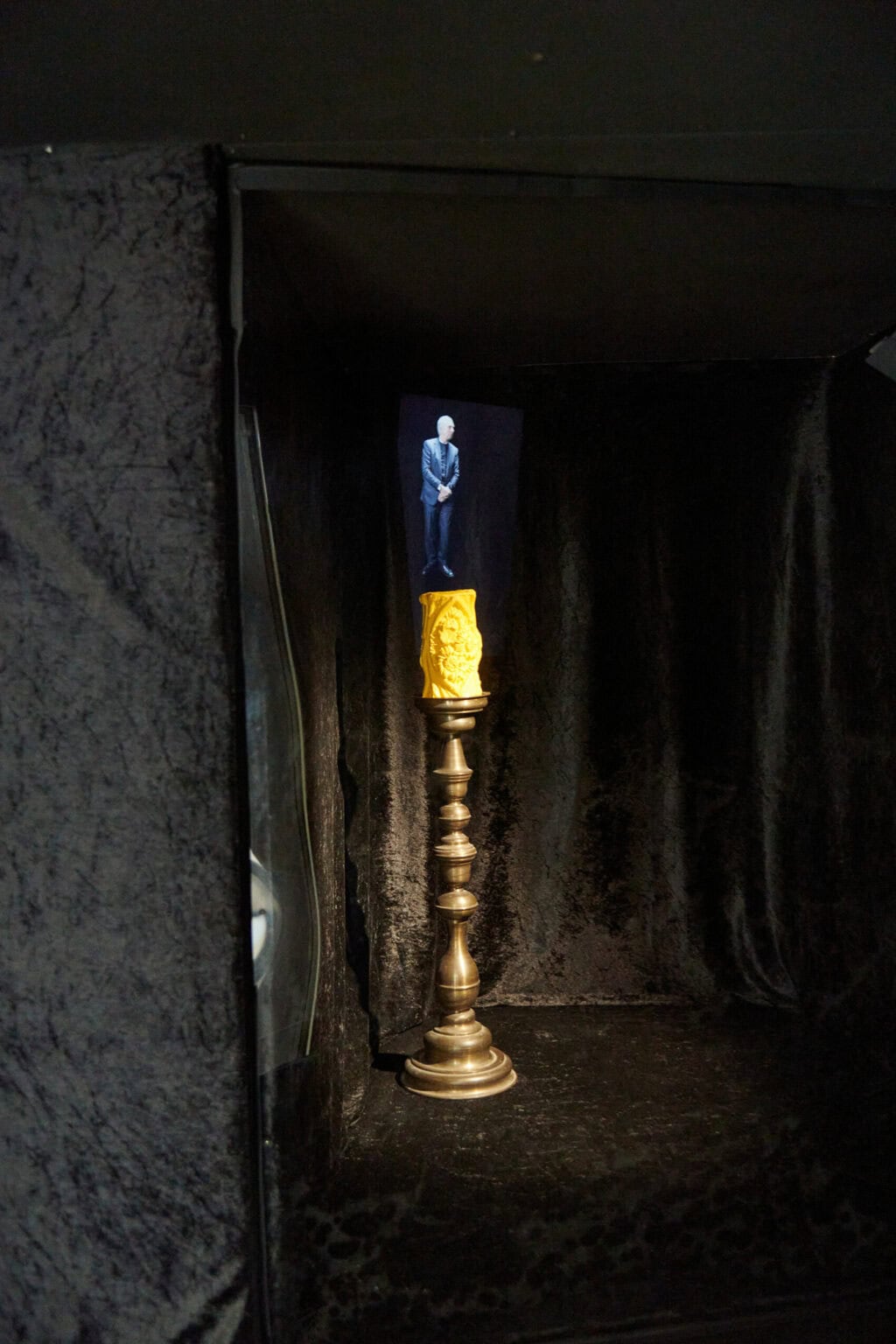 Foto: Ansicht eines abgedunkelten Raumes mit dunklem Boden. Die Wände sind mit schwarzem textil abgehangen. Im Raum steht ein aus unterschiedlichen Materialien bestehendes Objekt.