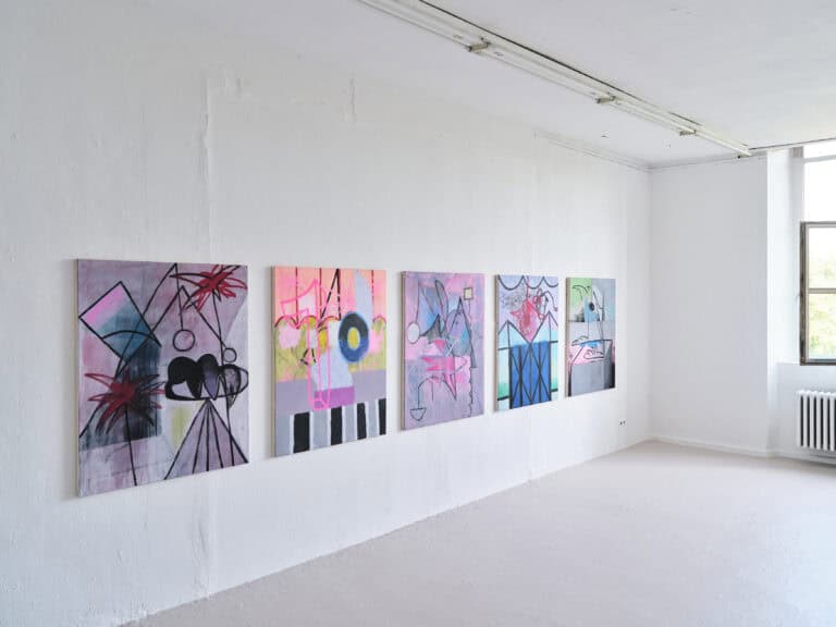 Foto: Aufnahme eines Ausstellungsraums mit weißen Wänden, grauem Boden und Fenster. An der linken Wand hängen fünf gleichgroße abstrakte bunte Gemälde.