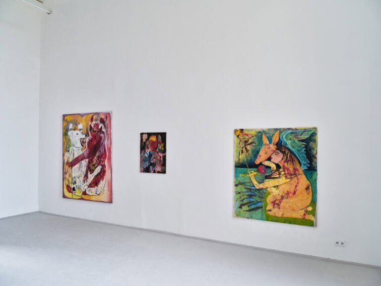 Foto: Aufnahme eines Ausstellungsraums mit weißen Wänden und grauem Boden. An der Wand hängen drei abstrakte bunte Gemälde.