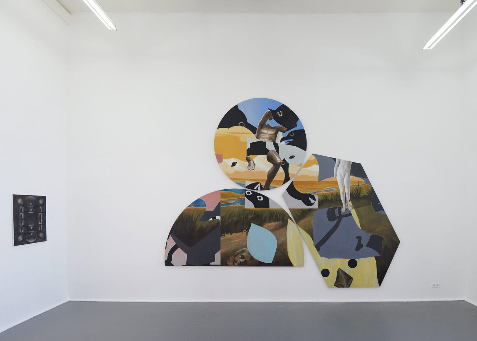 Foto: Ansicht eines Raumes mit weißen Wänden und grauem Boden. An den Wänden befinden sich Arbeiten auf Leinwand. Eine von Ihnen hat ein rechteckiges Format, die andere drei Leinwände sind als Gruppe unter- und nebeneinander gehangen und haben die Form eines Halbkreises, eines Sechsecks und eines Kreises.