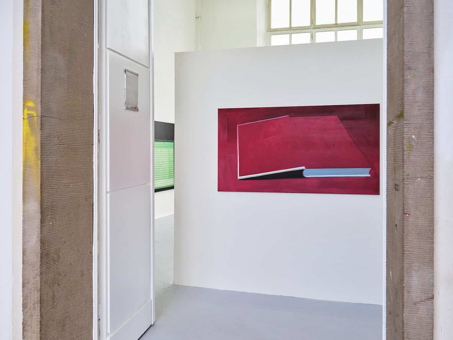 Foto: Ansicht eines geöffneten Tür mit steinerner Rahmung. Zu sehen ist eine niedrige Wand in einem Raum mit grauem Boden, auf der eine Leinwandarbeit hängt.