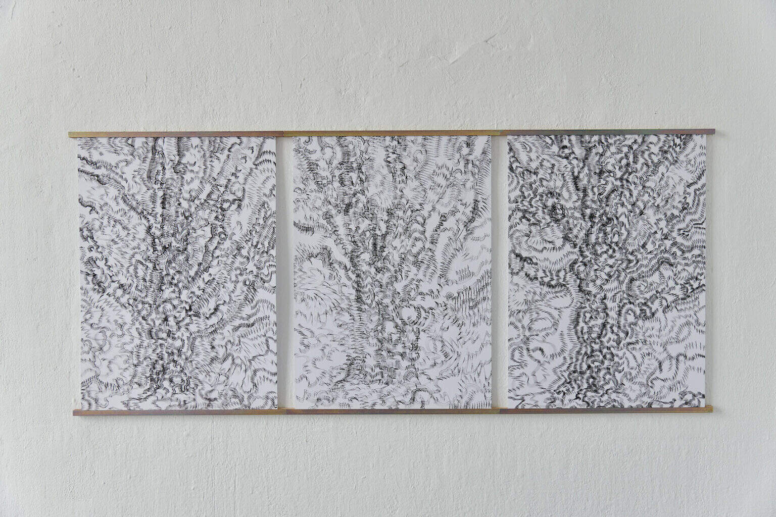Foto: Nahaufnahme von drei Papierarbeiten, die mit Leisten an einer weißen Wand fixiert sind.