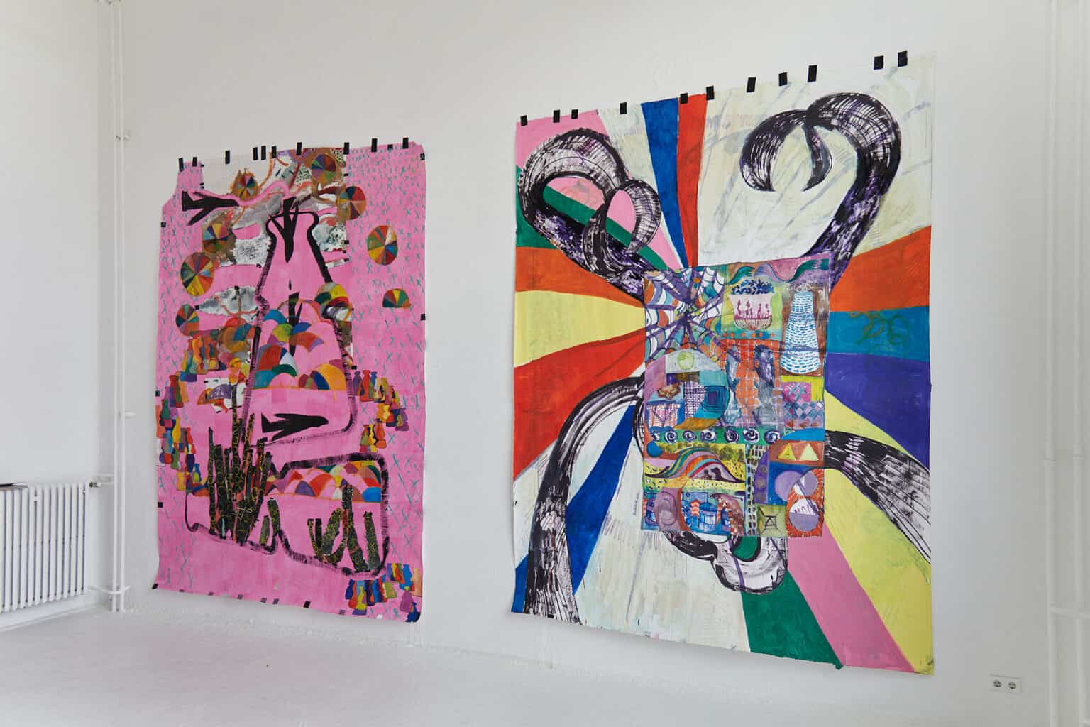 Foto: Ein Raum mit weißen Wänden und weißem Boden. An der Wand zwei flache, mit Farbe bearbeitete Papier in einem ähnlichen Format. Sie sind mit vielen Stücken schwarzem Tape an der Wand befestigt.