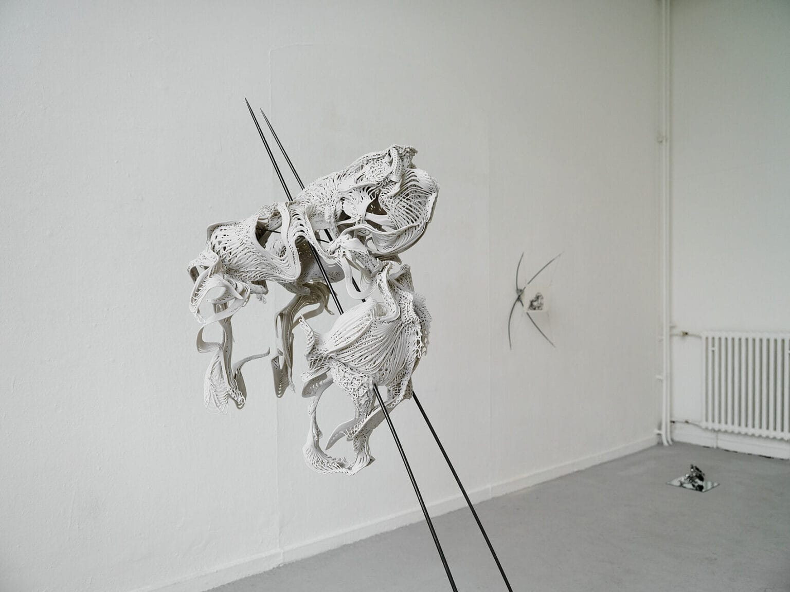 Foto: Ansicht eines Raumes Mmit weißen Wänden und grauem Boden. Im Raum verteilt, auf dem Boden und an den Wänden, befinden sich Objekte aus verschiedenen Materialien.