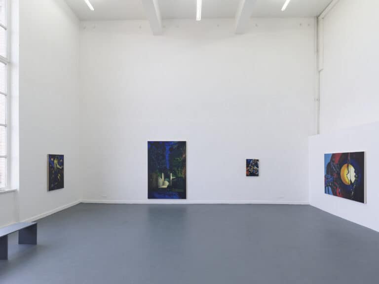 Foto: Aufnahme eines Ausstellungsraums mit weißen Wänden, grauem Boden und einem großen Fenster. An den Wänden hängen vier unterschiedlich große Gemälde. Eine Bank steht vor dem Fenster.