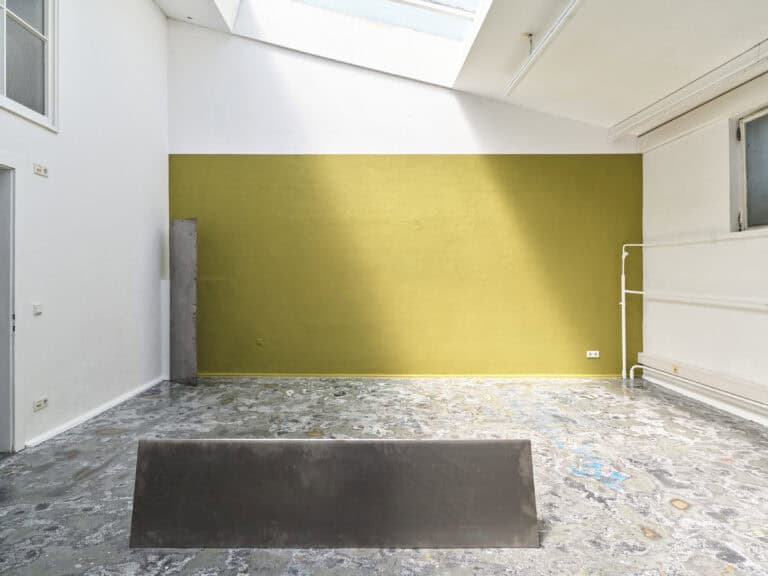 Foto: Aufnahme eines Ausstellungsraums mit Dachfenstern und abstrakter Kunstinstallation vor gelbgoldener Wand.