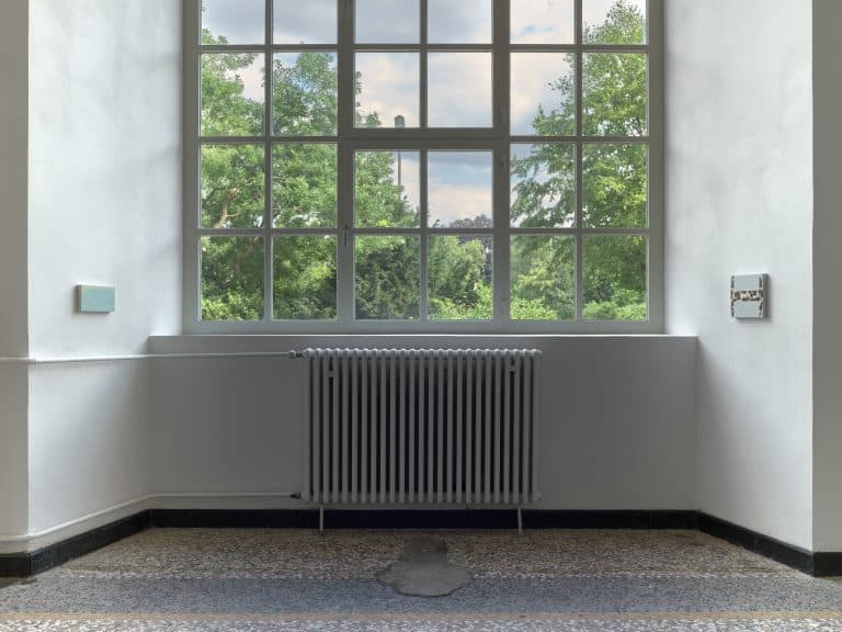 Foto: Aufnahme eines Ausstellungsraums mit einem großen Fenster. Rechts und links von dem Fenster ist jeweils ein kleinformatiges Bild gehängt.