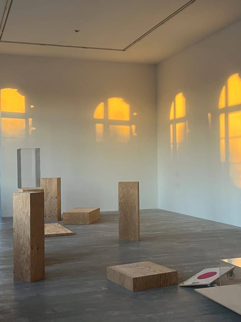 Heller Ausstellungsraum mit minimalistischen Skulpturen und warmem Sonnenlicht, das durch die Fenster fällt.