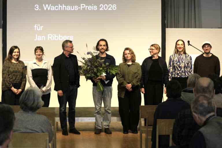 Foto: Personen auf einer Bühne. Eine Person in der MItte mit Blumenstrauß.