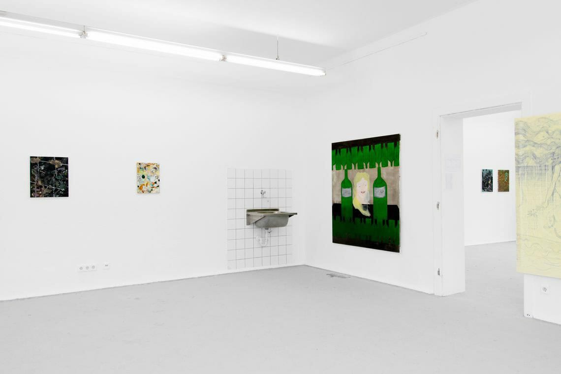 Foto: Ein Raum mit weißen Wänden und grauem Boden. An den Wänden hängen mehrere Leinwände in Klein- und Großformaten nebeneinander.