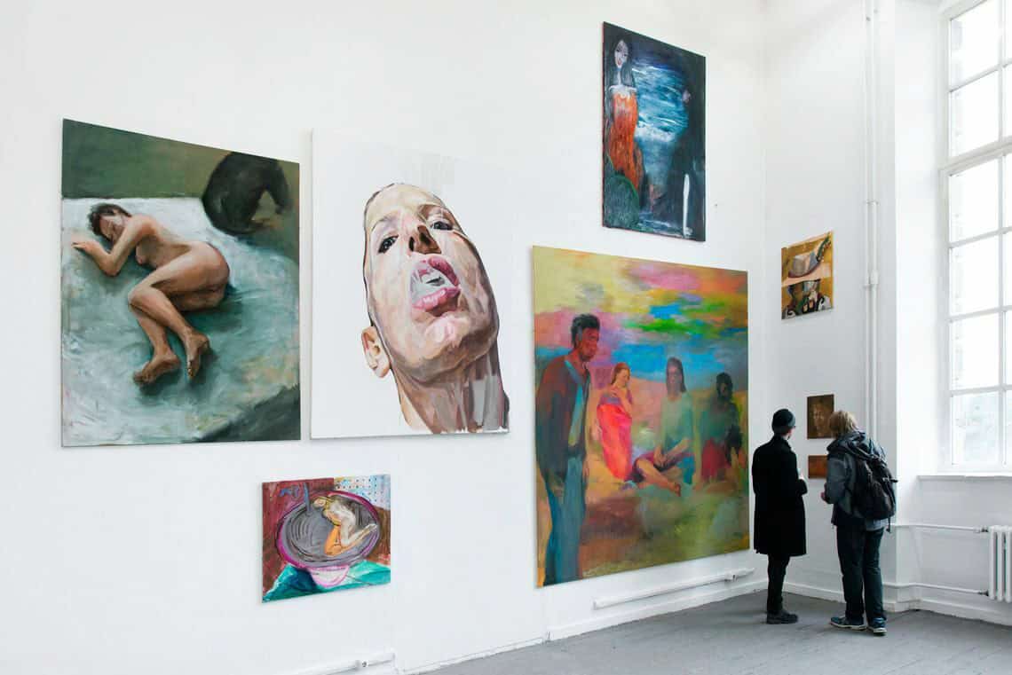 Foto: Ein Raum mit weißen Wänden und grauem Dielenboden. An den Wänden hängen mehrere Leinwände in unterschiedlichen Formaten neben- und untereinander.