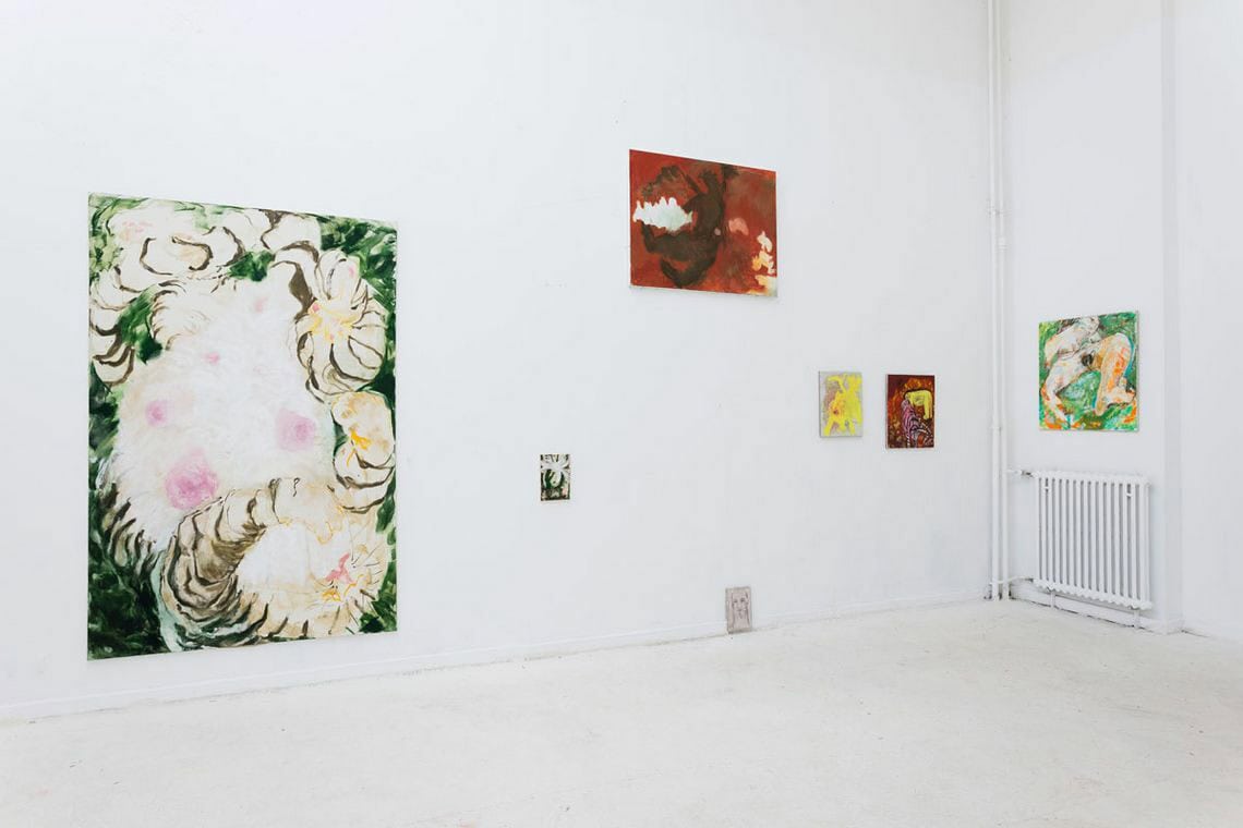 Foto: Ein Raum mit weißen Wänden und hellgrauem Boden. An den Wänden hängen, neben und übereinander, Leinwände in unterschiedlichen Formaten.