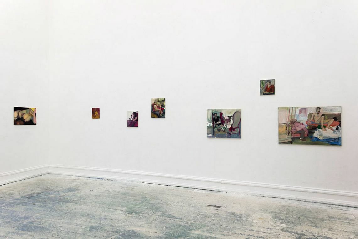 Foto: Ein Raum mit weißen Wänden und gräulichem Boden. An der Wand klein- und mittelformatige Arbeiten auf Leinwand auf unterschiedlicher Höhe gehangen.