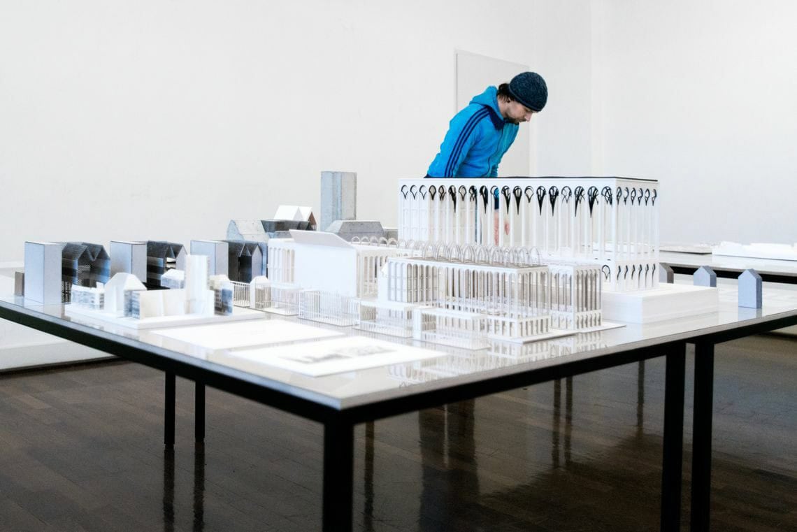 Foto: Ein Raum mit weißen Wänden und braunem polierten Dielenboden. Im Raum steht ein Tisch, auf dem sich modellartige Objekte und Papiere hinter Glasplatten befinden. Im Raum steht ein Mensch.