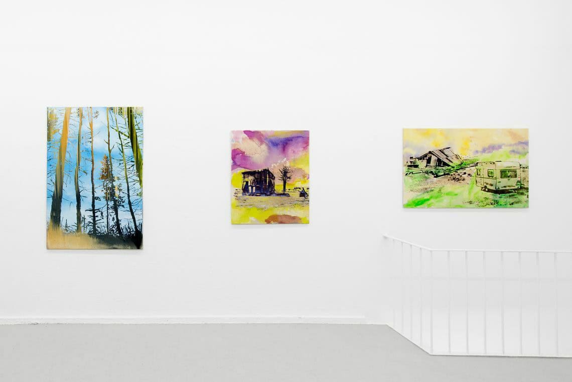 Foto: Ein Raum mit weißen Wänden und grauem Boden. An der Wand hängen drei mittelformatige Leinwandarbeiten auf ähnlicher Höhe.