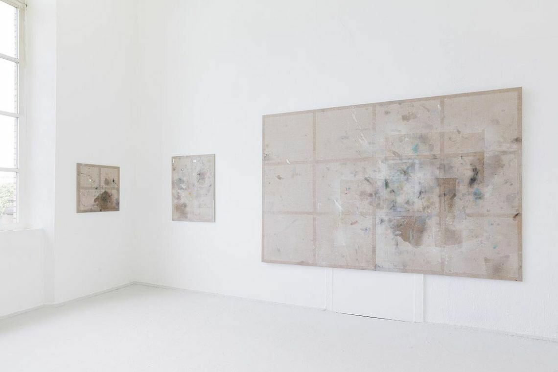 Foto: Ein Raum mit weißen Wänden, hellgrauem Boden und einem Fenster. An den Wänden hängen drei bespannte Keilrahmen im Klein-, Mittel und Großformat.