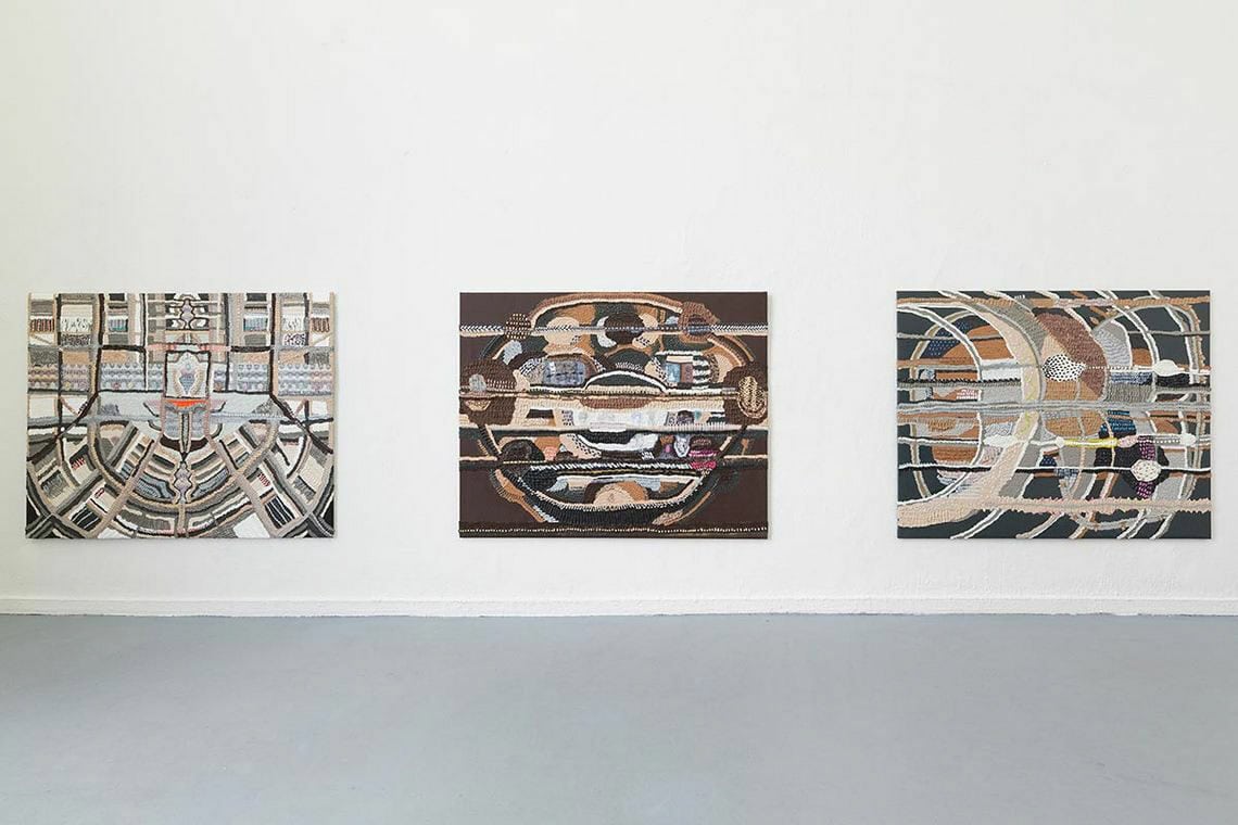 Foto: Ein Raum mit weißen Wänden und grauem Boden. An der Wand befindet sich drei großformatige, flache Objekte. Sie haben das gleiche Format und hängen im gleichen Abstand zueinander auf einer Linie.