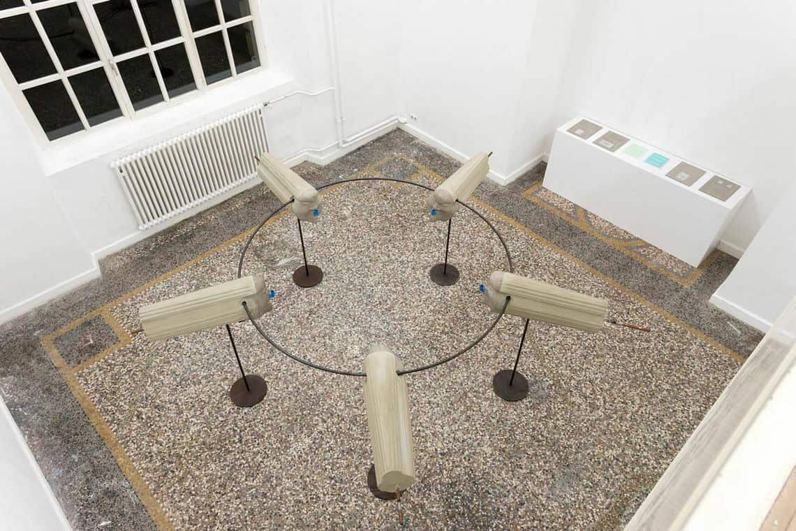 Foto: Ein Raum mit weißen Wänden und mehrfarbigem Steinboden aus Vogelperspektive. Im Raum befindet sich eine große Konstruktion aus Objekten, die einen Kreis bildet. Im Raum steht außerdem ein längliches, weißes Podest, auf dem Objekte liegen.