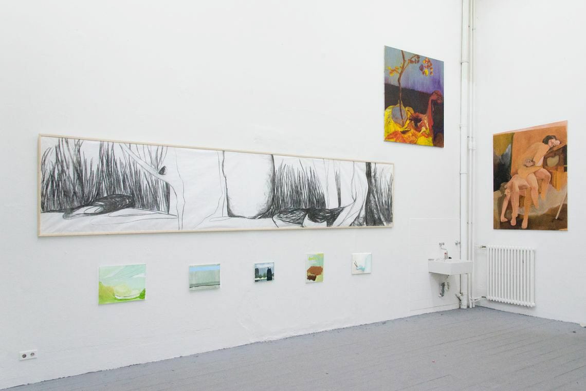 Foto: Ein Raum mit weißen Wänden und grauem Dielenboden. An den Wänden hängen mehrere Leinwände und ein gerahmtes Objekt in Klein-, Mittel- und Großformaten neben und übereinander.