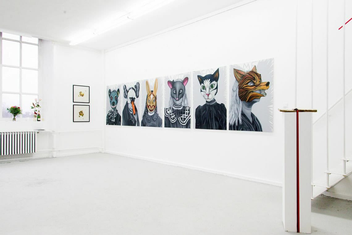 Foto: Ein Raum mit weißen Wänden, hellgrauem Boden und einem Fenster. An der Wand befinden sich mehrere Leinwände im gleichen Format, die auf gleicher Höhe im gleichen Abstand zueinander hängen. Daneben hängen zwei gerahmte Objekte im gleichen Format in einer Linie untereinander. Im Raum steht eine Skulptur, auf der Fensterbank stehen Blumen.