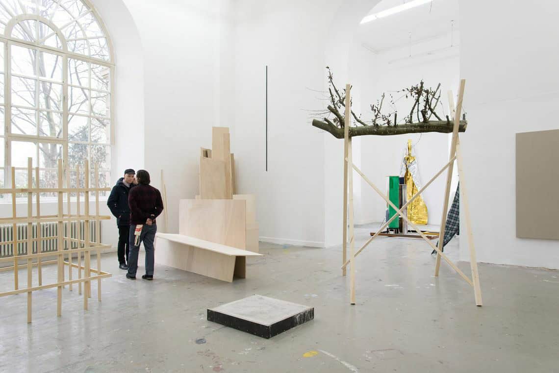 Foto: Ein Raum mit weißen Wänden, grauem Boden und einem großen Fenster. Im Raum befinden sich mehre große Skulpturen aus unterschiedlichen Materialien. An der Wand befinden sich ebenfalls Objekte.