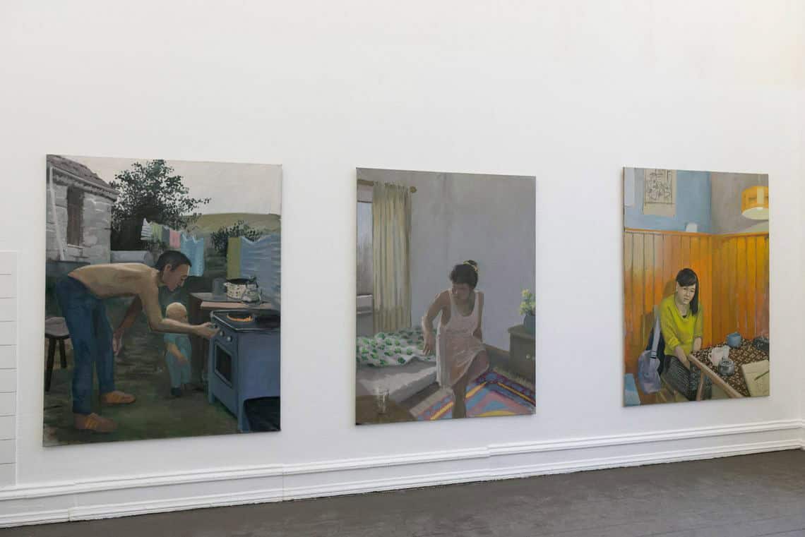 Foto: Eine weiße Wand und ein grauer Boden. Auf der Wand befinden sich drei großformatige, ähnlich große Leinwandarbeiten.