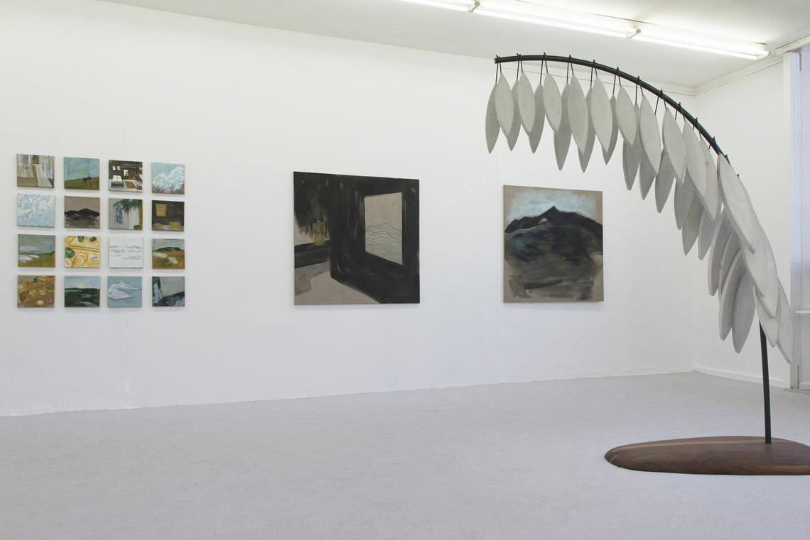 Foto: Ein Raum mit weißen Wänden und grauem Boden. An den Wänden hängen zwei großformatige Leinwände. Daneben hängt eine in einem Raster angeordnete Gruppe kleinformatiger Leinwandarbeiten, die in der Fläche ähnlich groß sind wir die daneben hängenden Großformate. Im Raum steht eine Skulptur.