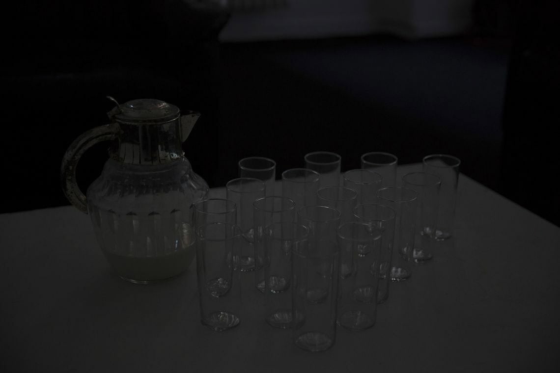 Foto: Eine Gruppe von Gläsern und eine gläserne Karaffe, die mit Flüssigkeit gefüllt ist, in einem dunklen Raum.