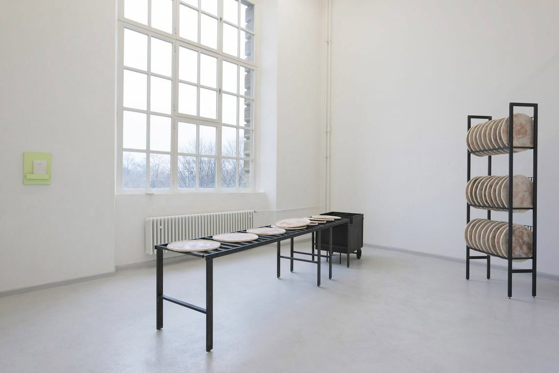 Foto: Ein Raum mit weißen Wänden, hellgrauem Boden und einem großen Fenster. An der Wand hängt ein kleinformatiges Objekt neben dem Fenster. Im Raum stehen zwei Skulpturen.